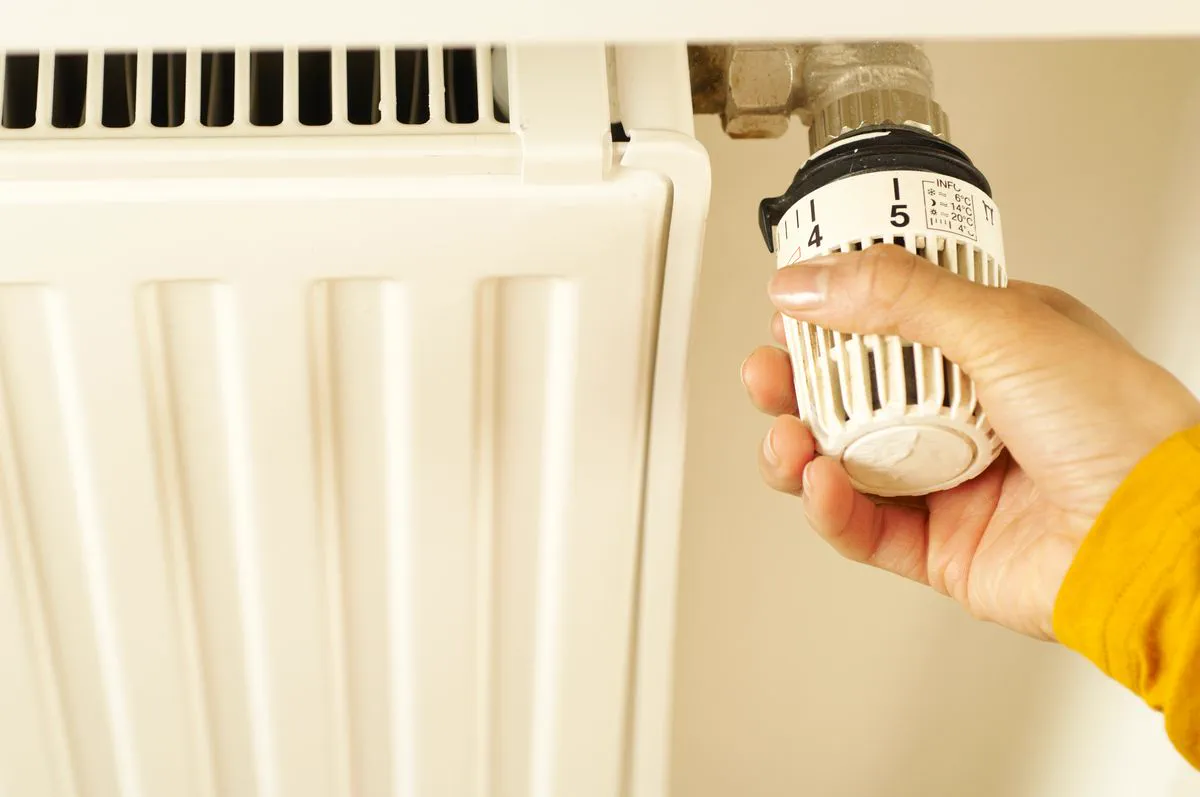 Hand turning the thermostat knob on a radiator