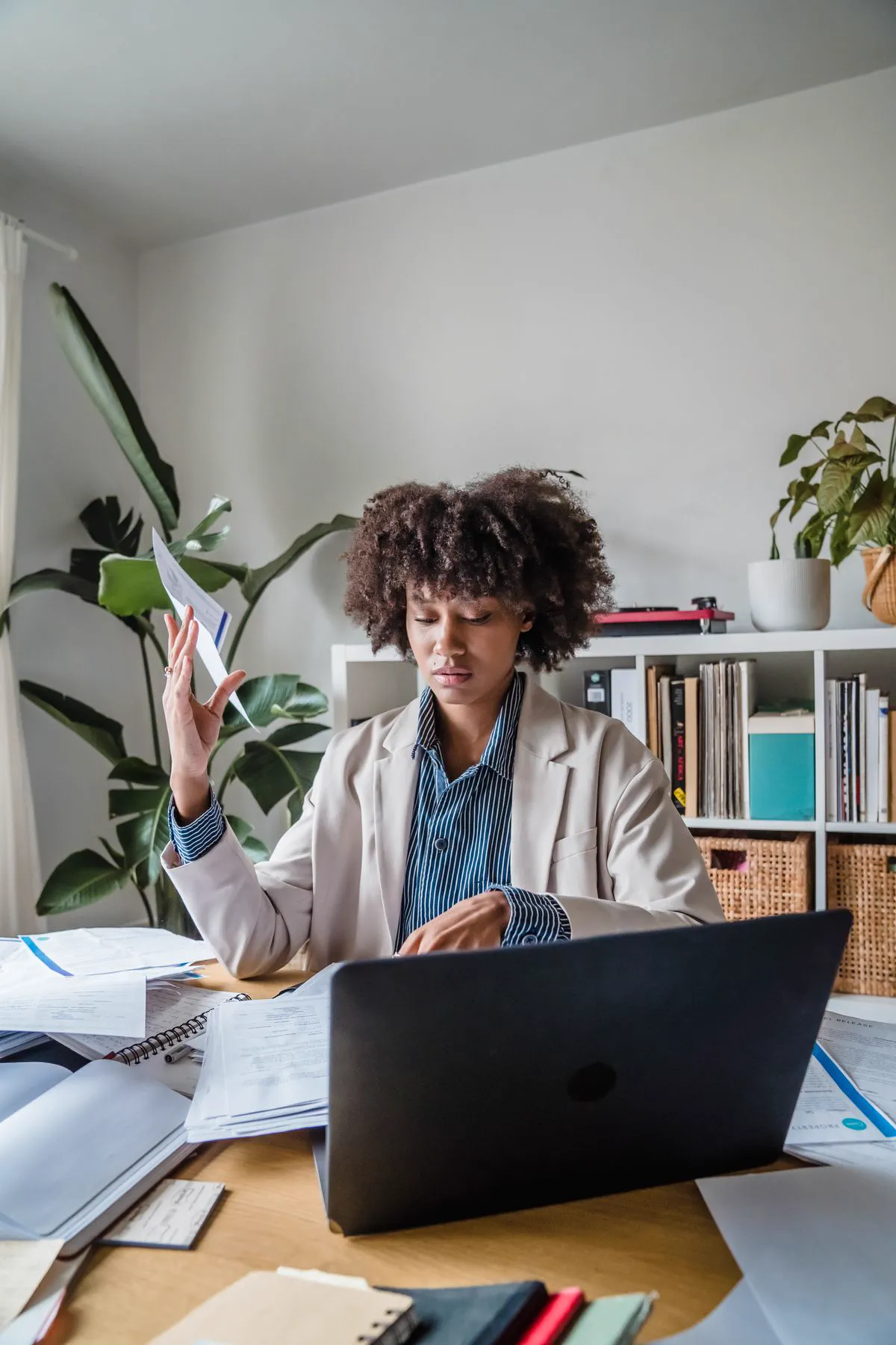 Woman at a desk covered in papers, with a laptop in front of her